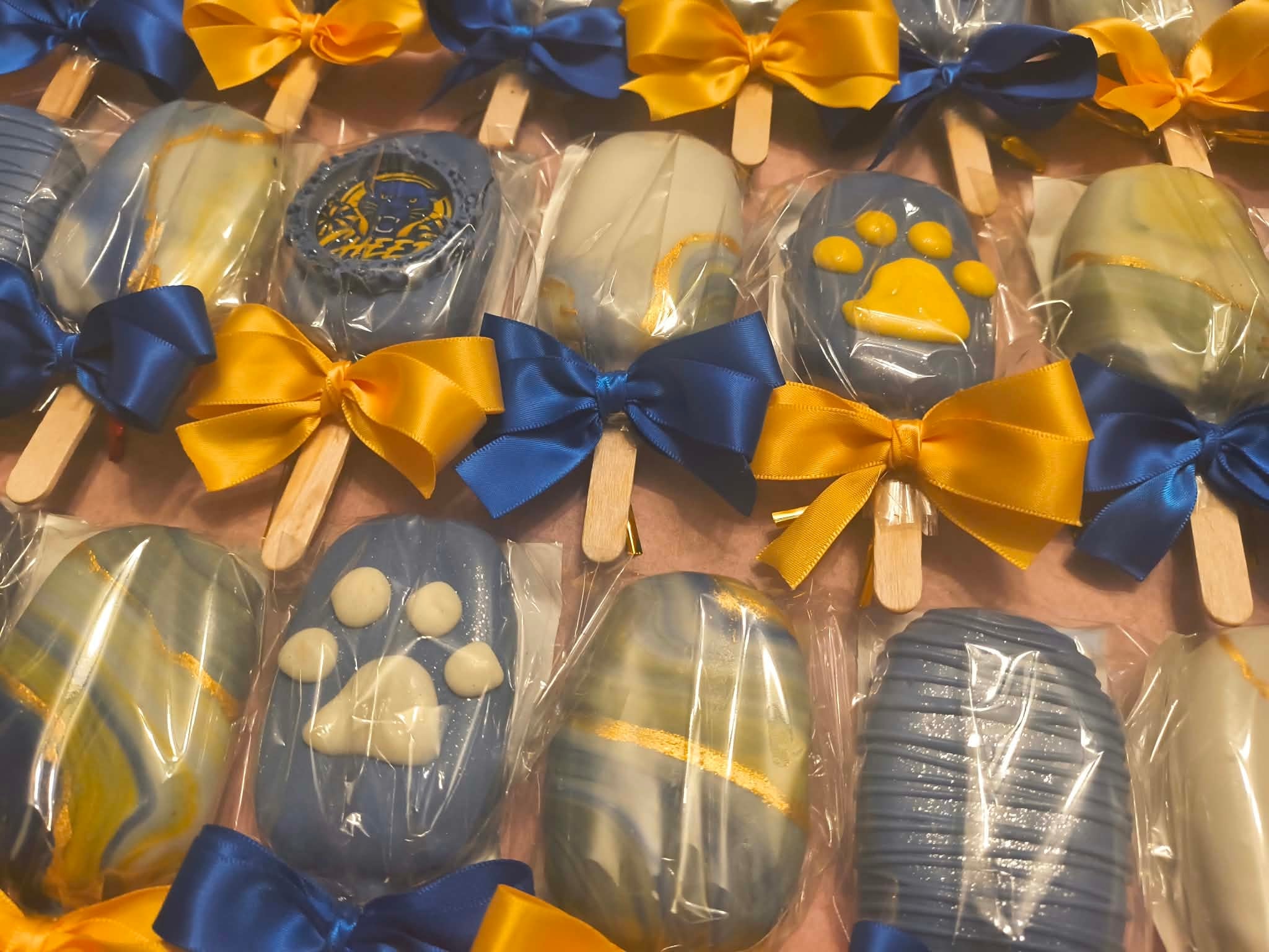 Decorated chocolate cakesicles with blue and gold bows